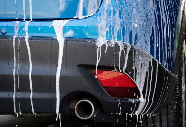 Blue car wash with white soap foam and professional auto care service. Car cleaning service concept. Vehicle cleaning service. Foam wash car detailing. Blue luxury SUV car is covered with white foam.