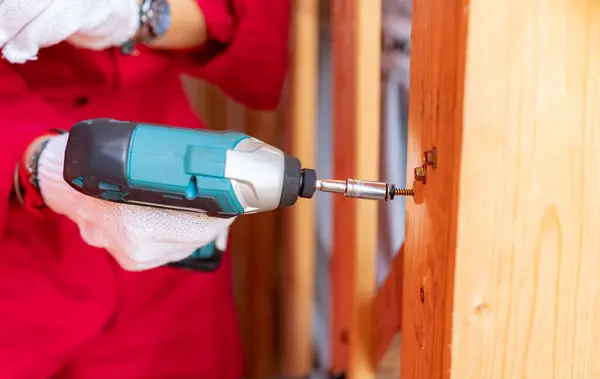Carpenter and screwdriver hand tool. A skilled worker set to work drilling and installing wooden fixtures, using electric screwdriver to construct and repair parts of house with precision and care.