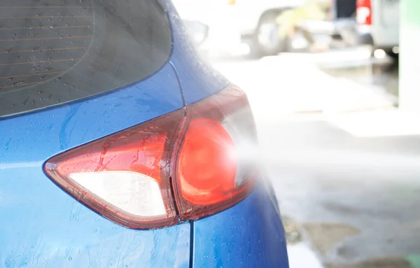 Car washing with high pressure water spray. Car cleaning. Auto care service concept. Vehicle cleaning. High pressure water spraying on tail light of blue car. Manual car wash with high pressure water.