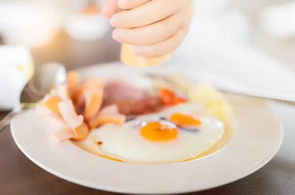Breakfast at hotel. Healthy meal was served on a beautifully set table at the hotel restaurant in the morning. The handcrafted breakfast. Fried eggs and sausage on white plate. Hand holding condiments