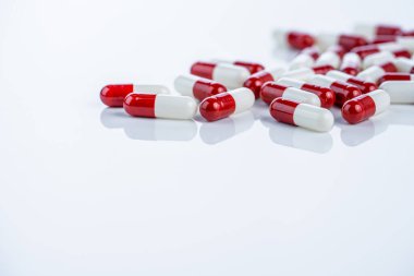 Beyaz arka plana saçılmış kırmızı beyaz kapsüller laboratuardan pazara uyuşturucu keşfi yolculuğunu gösteriyor. İlaç yenileme süreci ve yeni ilaçlar için sıkı onay aşamaları.