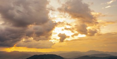Gün doğumunda, turuncu gökyüzü ve huzurlu dağ sırasının üzerindeki yumuşak bulutlarla birlikte doğa manzarası. Sakin bir sabah sahnesi. Şafağın güzelliği ve doğanın sükuneti. Huzurlu bir manzara. Huzur güne başlıyor.