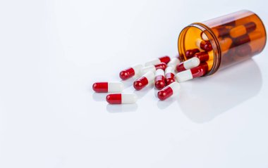 Plastik bir kutudan kırmızı ve beyaz reçeteli kapsüller dökülüyor. Düzenli farmasötik ilaçlar. Sağlık sektöründe güvenlik standartlarını, ilaç verimliliğini ve hastanın refahını vurgulamak.