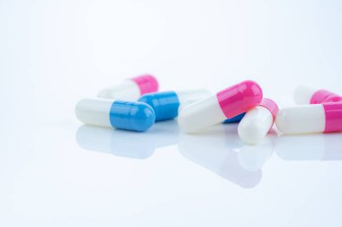 Beyaz arka plana yayılmış mavi ve pembe kapsül hapları, ilaç ürünlerinin sergilenmesi, sağlık hizmetleri kavramları ve reçeteli ilaçların ilerlemekte olan tedavi ve hastanın refahında rolü.