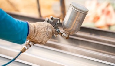 İnşaat işçisi inşaat alanında sprey tabancayla metal yapı yüzeyini boyuyor. Metal aşınma ve pas koruması. Endüstriyel hassasiyet. Metal bir yapıya koruyucu kaplama.