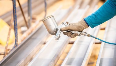 İnşaat işçisi inşaat alanında sprey tabancayla metal yapı yüzeyini boyuyor. Metal aşınma ve pas koruması. Endüstriyel hassasiyet. Metal bir yapıya koruyucu kaplama.