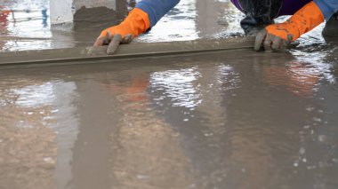 Mason işçisi inşaat alanındaki beton zeminde malayla çalışıyor. İnşaat işçisi ıslak betonu döşeme zeminine döşemiş. Temel ve döşeme görevleri.