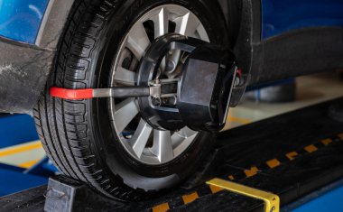 Wheel alignment equipment grip the tire of car wheel in car repair shop. Auto wheel alignment in workshop of service station. Car wheel balance. Suspension adjustment. Vehicle inside garage workshop.