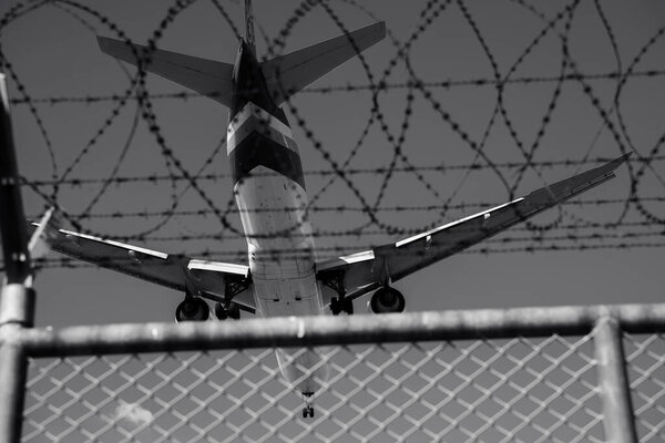 Airplane approaching barbed wire fence. Security, travel restrictions, and complexity of aviation transportation at airports. Security and freedom in air travel. Safety, boundaries, and transportation