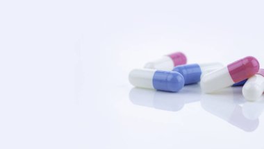 Beyaz arka plana yayılmış mavi ve pembe kapsül hapları, ilaç ürünlerinin sergilenmesi, sağlık hizmetleri kavramları ve reçeteli ilaçların ilerlemekte olan tedavi ve hastanın refahında rolü.