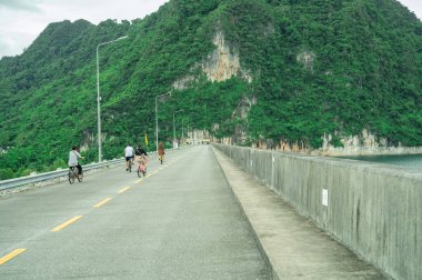 Öğleden sonra çevresi kireçtaşı kayalıklarıyla çevrili beton bir baraj üzerinde birlikte bisiklet süren aile, çevre dostu turizmi, sürdürülebilir seyahat ve aktif açık hava yaşam tarzını destekliyor..