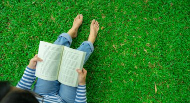 Taze yeşil çimenlerde çıplak ayakla oturmuş kitap okuyan bir kadın. Dijital detoks inzivası, zihinsel sağlık ve kişisel bakım. Farkındalık. Zihinsel sağlık dengesi, rahatlama ve teknolojisiz geri çekilme tarzı..