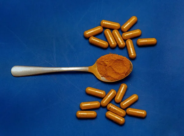 Turmeric food supplement pills with curcumin seasoning powder in metal spoon isolated on blue background