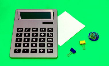 Boş kağıt notlu dijital elektronik hesap makinesi ve renkli metal ataç yığını gibi diğer ofis malzemeleri sabit.