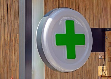 Eczane yeşil haç işareti caddedeki bir binanın cephesine asılmış.