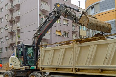Kazı makinesi, Kentsel caddedeki inşaat alanındaki çöp kamyonuna toprak yüklüyor.
