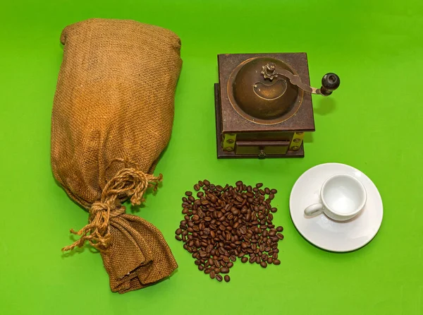 Pile of raw coffee beans with burlap sack and grinder on sides
