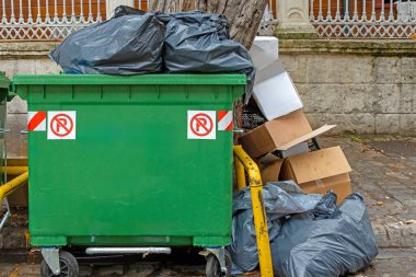 Sokakta plastik bir konteynırın yanında duran çöp yığını.