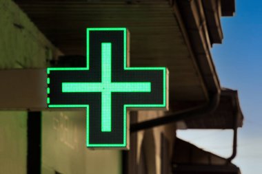 Eczane yeşil parlıyor ve sokak binasının ön cephesinde tabela var.