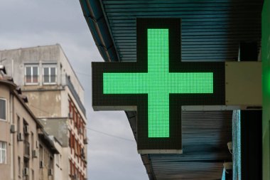 Dışarıdaki binanın ön cephesinde parlak, parlayan eczane işareti var.