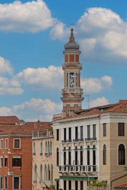 Arka planda mavi gökyüzü bulutları olan eski Venedik evinin çatısında uzun bir kule.