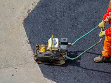 Male industrial worker using plate compactor tool outside on street asphalt clipart