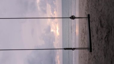 Tayland 'da hindistan cevizi ağacı ve güneşli yaz havası ile beyaz kumsalın yanında salıncak dikey video günbatımı vanilya gökyüzü saati, deniz sahili manzarası