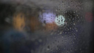 Yağmur fırtınasından gelen su damlacığı otobüsün içindeki cam pencerenin üzerinde, 4K üzerinde ışık saçan, soyut bir arka plan ile kentteki yolda sıkışıp kalmış.