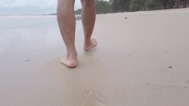 低い角度から見ると 人の足の動きが遅く 砂浜の白いビーチで海の水の波に沿って裸足で歩く スローモーションで水と泡のスプラッシュ 夏のビーチの休日の風景休暇 — ストック動画