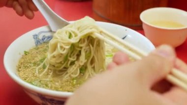 Tonkotsu soslu ramen eriştesini yemek çubuklarıyla al ve ayartmayı azaltmak için yukarı kaldır. Çin eriştesi. Japon ulusal Ramen kase sıcak çorbası.