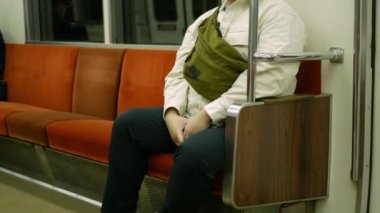 Japonya metrosu toplu taşımacılığında hareket ederken, Asyalı yolcu banliyö vagonunda oturuyor.