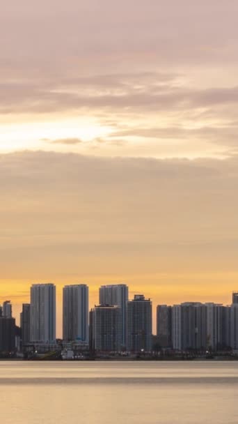 海岸近くに高層ビルが建ち並ぶウォーターフロント都市の縦長のタイムラプスシルエットバニラ黄昏の空と日没の時間帯空に雲が動く風景 — ストック動画