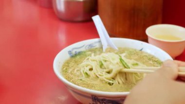 Asyalı adam Japon eriştesi yemek için çubuk çubuk kullanır. Domuz dilimli Japon fast food rameni.