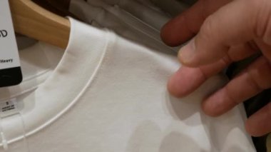 Closeup of Hands Plucked Hanger Choosing Clothes t shirt in a retail Clothing Store in a Shopping Mall. Sale Promotion and Shopping background Concept.