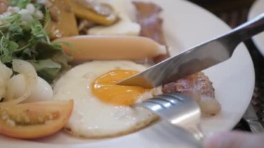Beyaz tabakta kızarmış yumurta yemek için çatal ve bıçak kullanarak yumurta sarısı keserek. Yumurta sarısı ve yumurta sarısı kesiyorum. Sağlıklı kahvaltı ya da öğle yemeği.