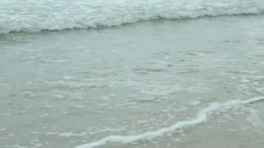 Beyaz kumsal yüzey dokusunu deniz dalgalarıyla görmek yaz güneşli bir günde sahile vurdu, dalgalar beyaz köpük dalgalarıyla kıyıya doğru sürüklendi, yaz tatili arka planında 4k videosu çekildi.