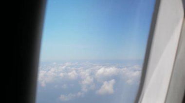 Uçarken açık mavi gökyüzü ile kabarık beyaz bulut üzerinde uçak penceresinden hava manzarası, doğal arka plan kavramı ile seyahat eden uçağın penceresinden görüntü