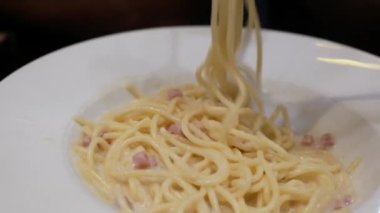 Akşam yemeği için ev yapımı spagetti beyaz soslu makarna yemek için çatal ve kaşık kullanmak, İtalyan mutfağı ev yapımı yemek yemek, kabaralı beyaz soslu makarna yemek.