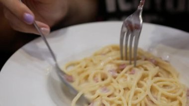 Akşam yemeği için ev yapımı spagetti beyaz soslu makarna yemek için çatal ve kaşık kullanmak, İtalyan mutfağı ev yapımı yemek yemek, kabaralı beyaz soslu makarna yemek.