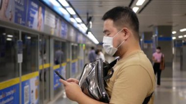 Asyalı genç adam metro istasyonunda yaklaşan treni beklerken 5 gramlık akıllı telefon kullanıyor. Teknoloji geçmişi olan Asyalı bir yolcu.