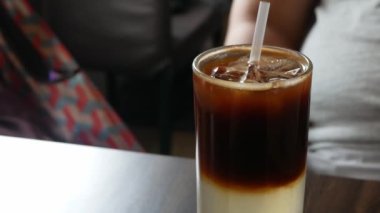 Tahta masadaki en küçük kafede samanla servis edilirken limon suyunun üzerinde bir bardak taze buzlu kahveye yakından bakın. Bir bardak buzlu içecek.