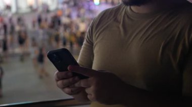Asyalı bir adamın gece vakti alışveriş alanında Zebra geçişi geçmişiyle seyahat ederken akıllı cep telefonu mesajları kullandığı görüntüsü. Şehir caddesinde renkli bokeh ile mesajlaşma