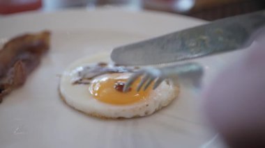 Beyaz tabakta kızarmış yumurta yemek için çatal ve bıçak kullanarak yumurta sarısı keserek. Yumurta sarısı ve yumurta sarısı kesiyorum. Sağlıklı kahvaltı ya da öğle yemeği.