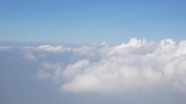 Uçakta uçarken, bulutların üzerinde uçan uçağın berrak mavi gökyüzü üzerindeki kabarık beyaz bulutun hava görüntüsü. Hava yoluyla seyahat eden uçağın penceresinden görünüm, doğal arka plan konsepti