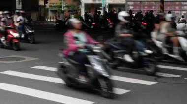 Taipei 'de gündüz vakti kalabalık bir motosiklet trafiği yaşanırken, kavşaktaki zebra kavşağındaki asfalt sokağa alçak açılı görüş.