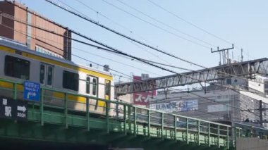December31,2019.Tokyo,Japan.view to the japan railway trackway with train commuter moving passing and background of advertising neon billboard on the building in daytime