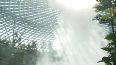 Gündüz vakti Singapur 'da tropikal yağmur ormanları olan modern gözlüklü kubbe tasarımı altında kapalı bir girdap şelalesine yakından bakın. Modern ev yapımı insan yapımı su dökülüyor.