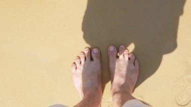 Düşük açı, çıplak ayakla sahile vuran deniz dalgalarıyla beyaz kumsalda hareket eden çıplak ayaklar, yaz tatili, doğal arka plan 4K. Kumsalda rahatça yürümek.