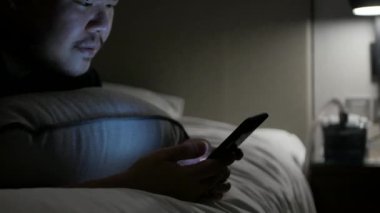 Asyalı adam cep telefonuyla sohbet ederken ve gece vakti yatakta uzanırken.