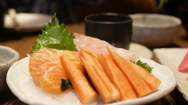 新鮮な生魚の日本料理のボウルに近い 箸を使って 氷の上からサーモンの刺身を選び 食べるために レストランで日本料理をダイニング — ストック動画
